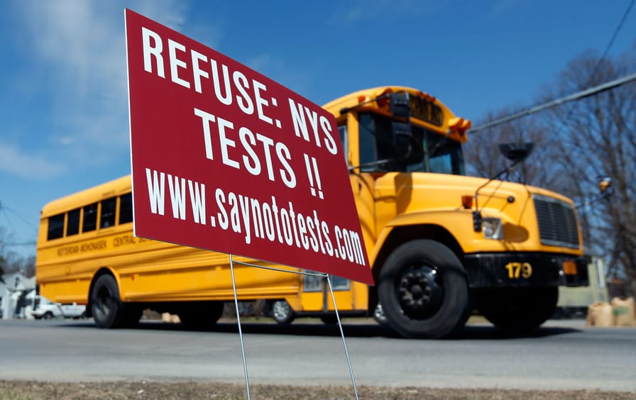 A school bus passes a sign encouraging parents to refuse that their children take state tests