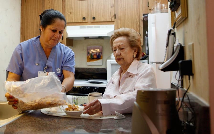 home health aide Maria Fernandez, left, pours cereal for Herminia Vega, 83.