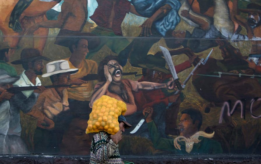 A man carries a sack of oranges while walking past a mural depicting a fight between farmers and private landlords in Tegucigalpa, Honduras's capital.