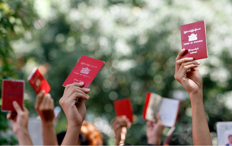 Myanmar nationals hold up their passports outside the embassy of Myanmar in Singapore