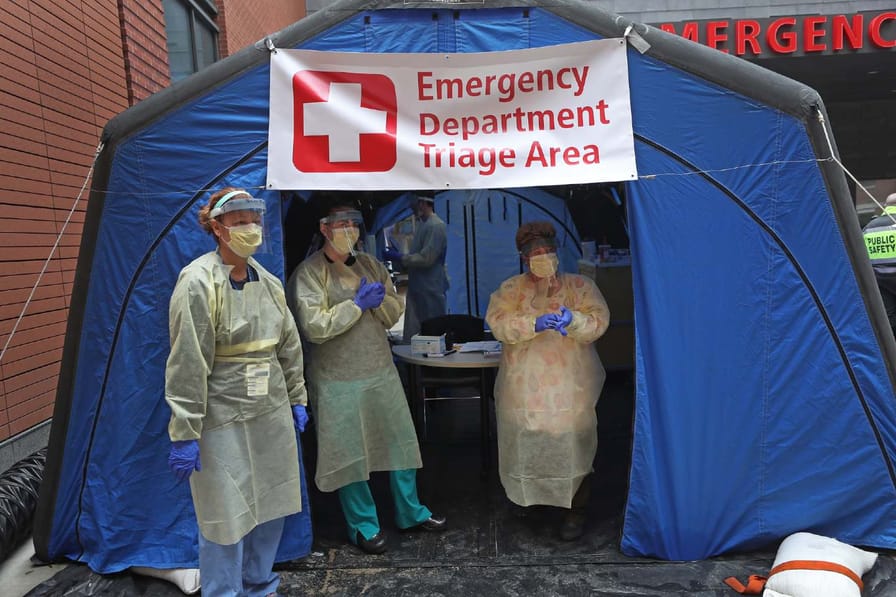 Nurses in protective gear stand outside a tent labelled 