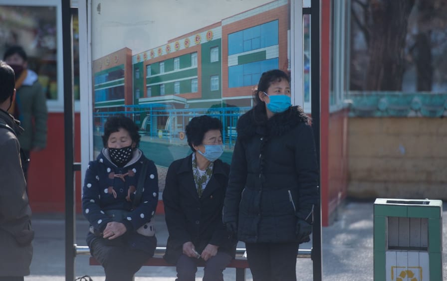 People in Pyongyang wait at a bus stop, wearing face masks.