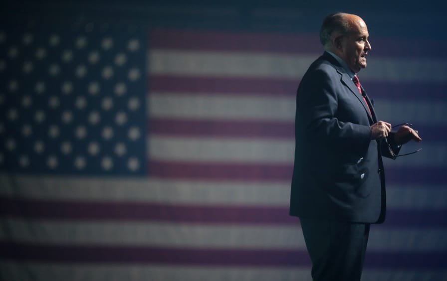 Rudy Giuliani standing and speaking in front of a US flag.