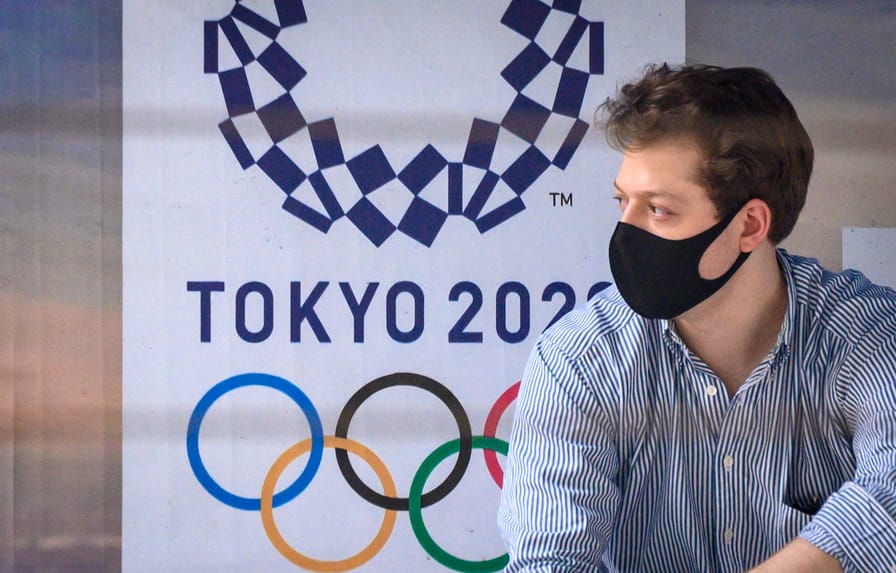 A man wearing a facemask sits in front of a Tokyo 2020 advertisement