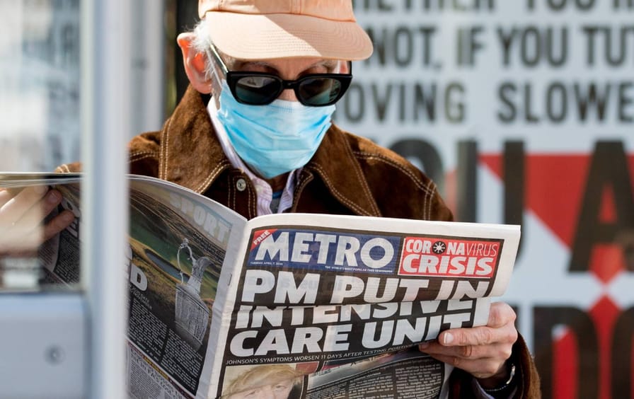 A man wearing a surgical mask reads the Metro newspaper