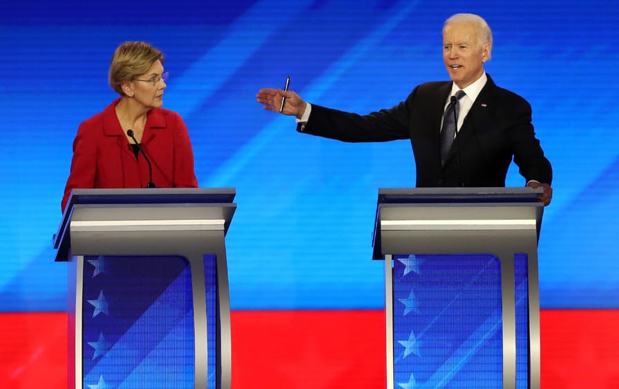 Elizabeth Warren and Joe Biden stand at their podiums at the presidential debate. Biden's hand is up, gesturing toward Warren.