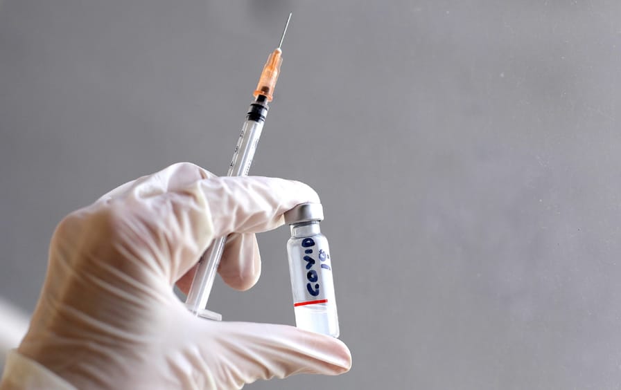 A gloved hand holds a syringe and a small vial of liquid marked 