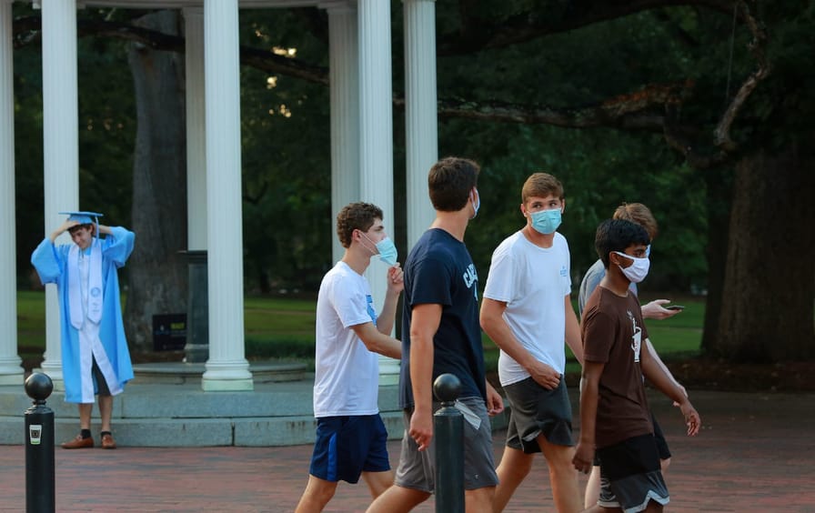 A group of five UNC freshman boys walk on campus wearing masks.
