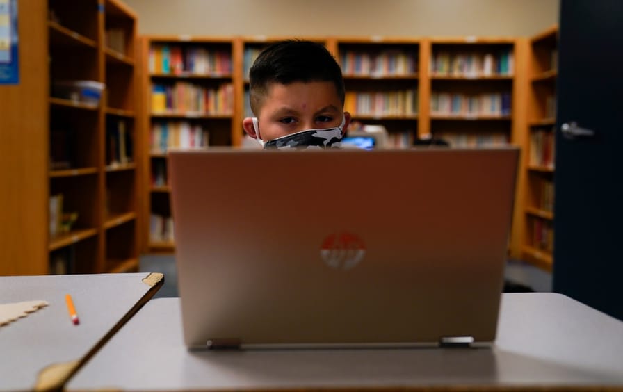 A young student sits in front of a laptop, attending an online class.