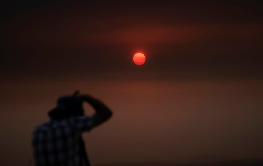 A man takes a photo of the sun in a blood orange sky during the West Coast fires