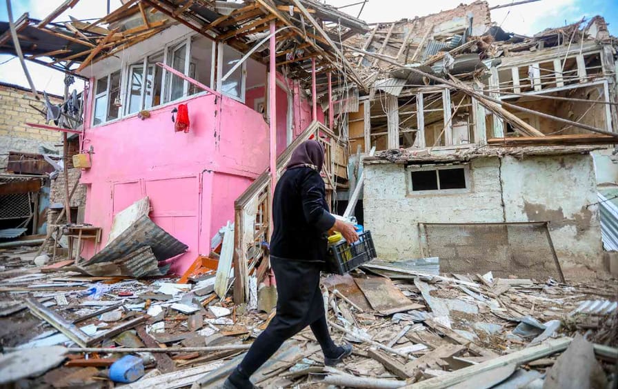 A woman walks past a severely damaged house surrounded by debris
