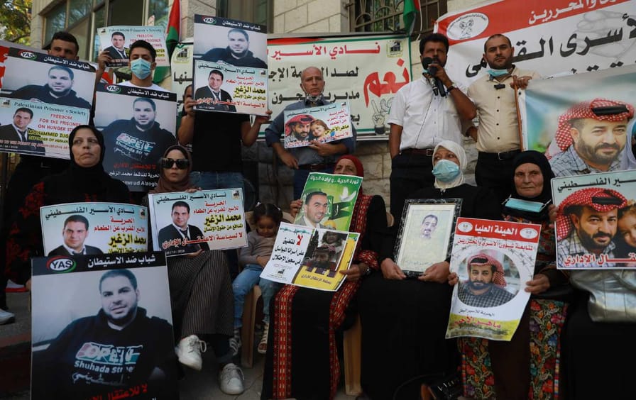 A crowd of people sit and stand holding posters, some bearing the picture of Maher al-Akhras.