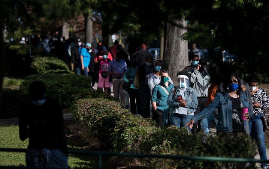 People wearing masks and face shields wait in a long line for early voting