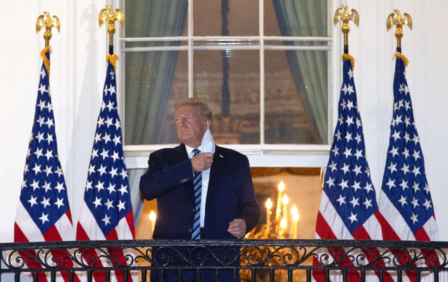 Donald Trump stands on the balcony of the White House taking off a surgical mask