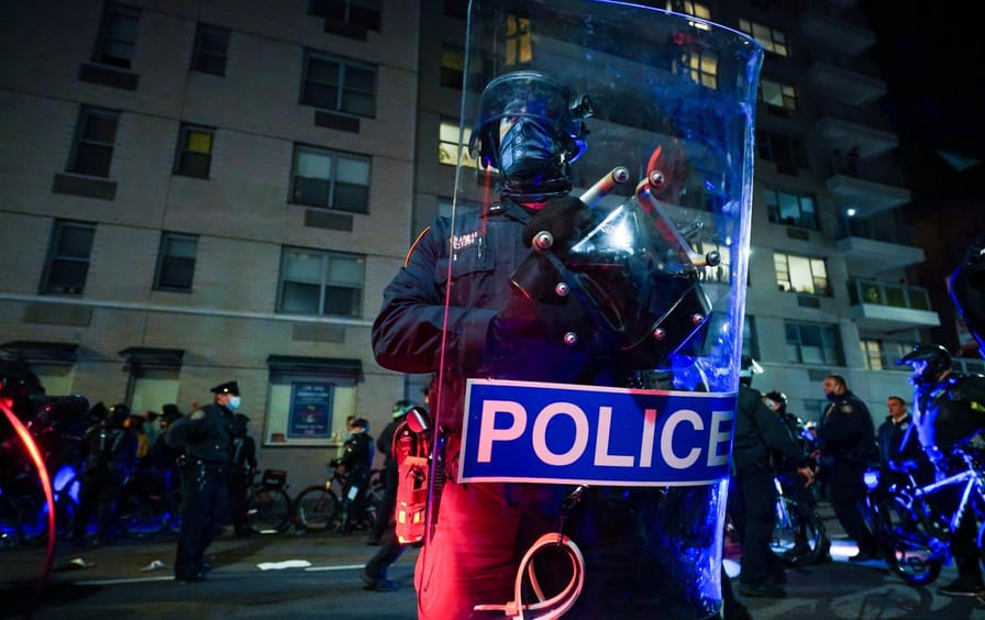 A police officer holds a riot shield that reads POLICE