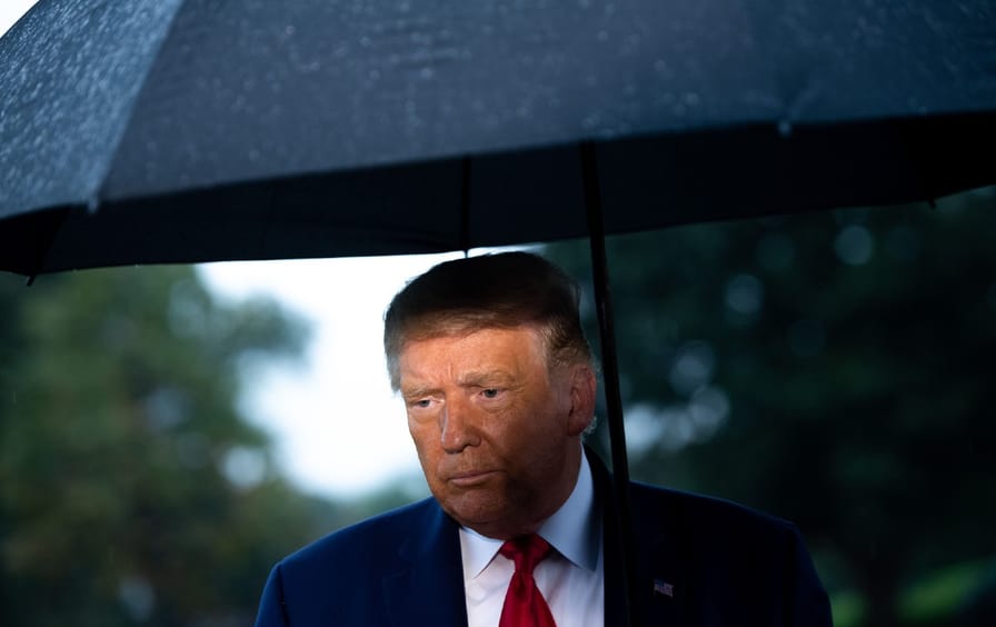 Donald Trump stands looking forlorn in the rain under a black umbrella