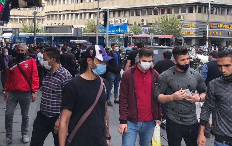 A group of people wearing face masks stand on a busy street.
