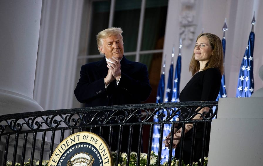 Trump and Amy Coney Barrett stand next to each other behind a gate.