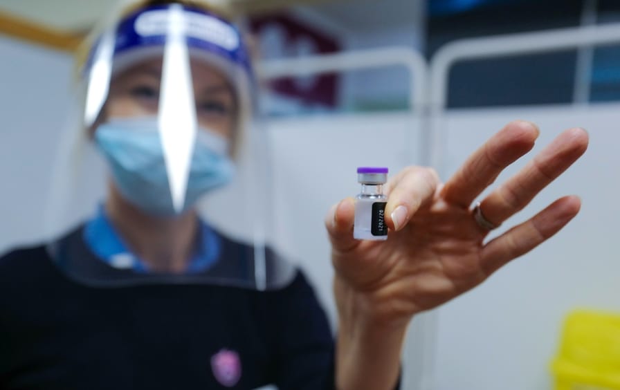A nurse wearing a surgical mask and face shield holds a vial of the Covid-19 vaccine