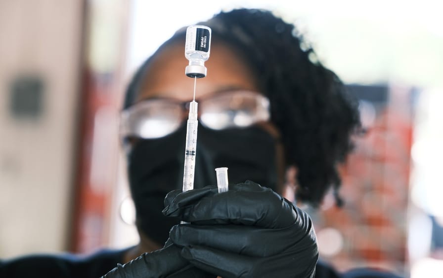 Woman holds up needle and vial of vaccine