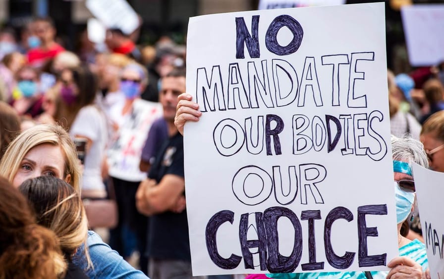Protest, with someone holding a sign reading NO MANDATE OUR BODIES OUR CHOICE