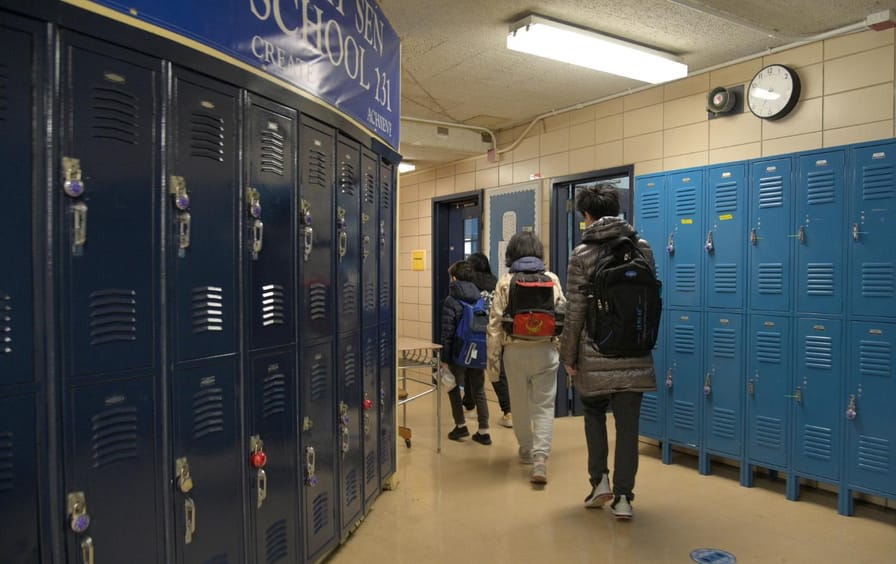 Students walk through a hallway lined with blue lockers.