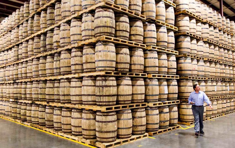 A man walks toward a corner formed by stacked whiskey barrels.