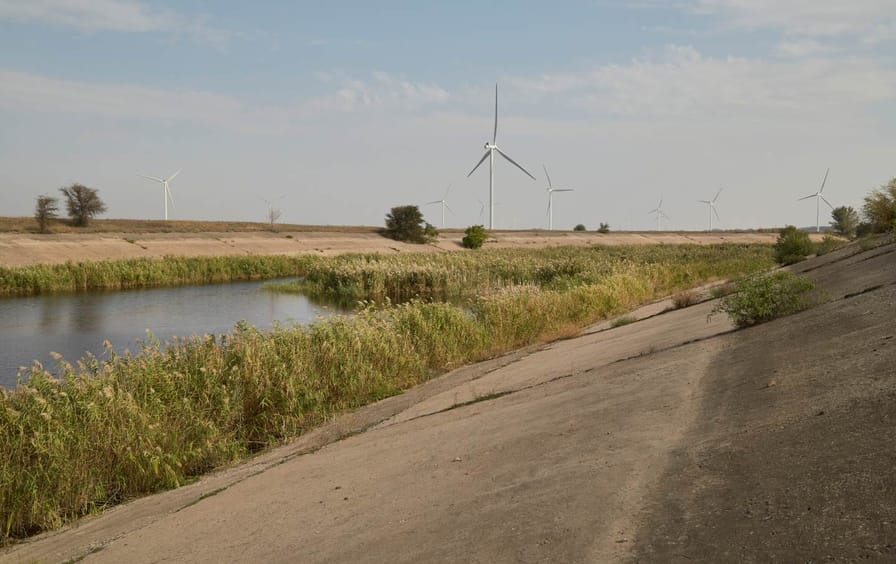 A low lying irrigation canal passes alongside a field of windmills