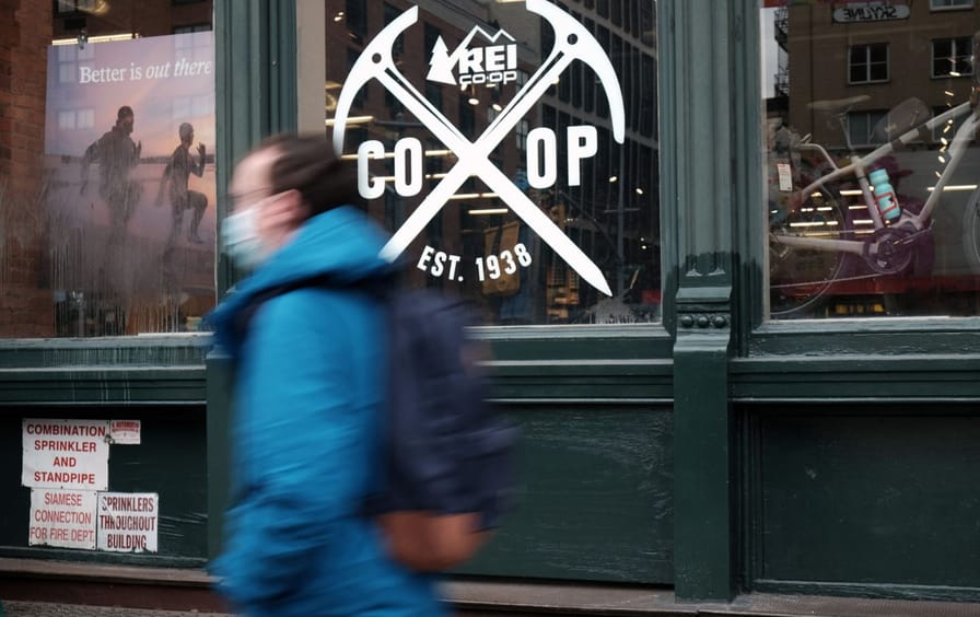 A man walks past a shop window with the REI logo on it,