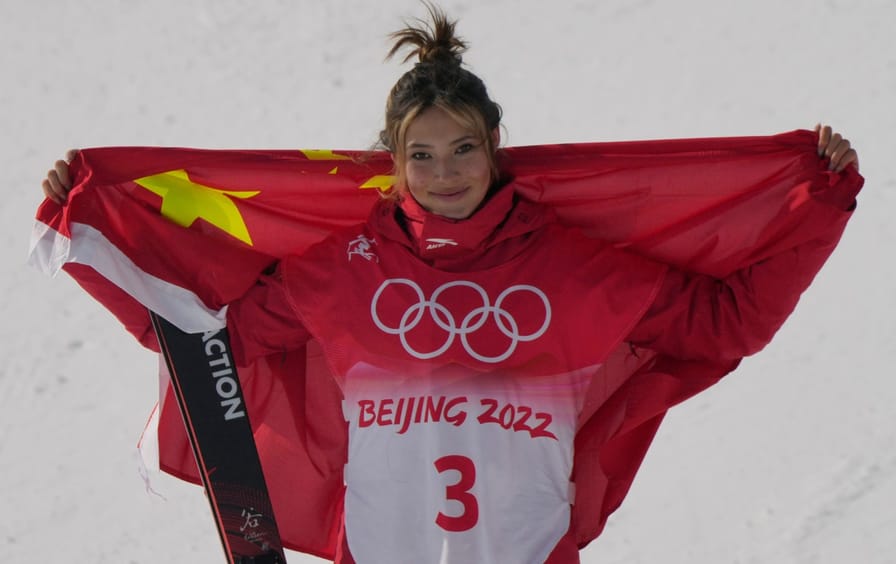 A young woman in a red uniform holds the Chinese flag above her shoulders and smiles