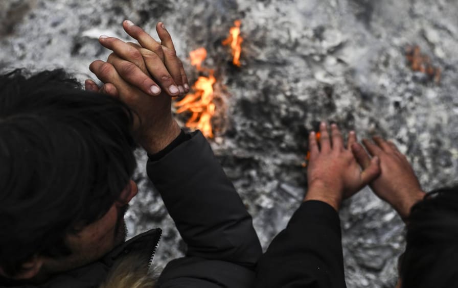 Two people warm their hands above a fire