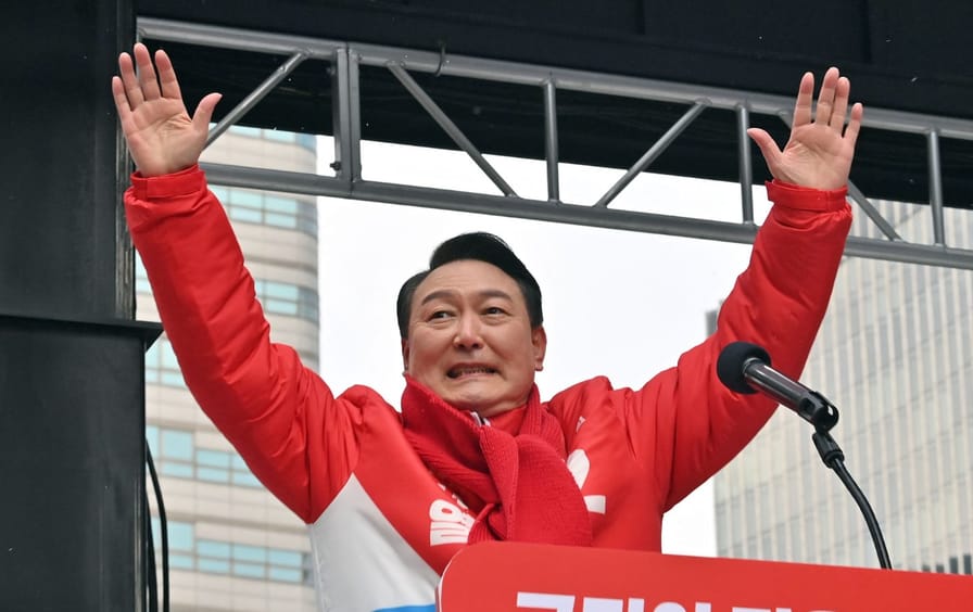 A man in a red jacket and scarf raises his hands above his head