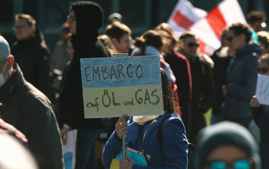 A person holds a sign the colors of the Ukranian flag with a slogan about an embargo of oil and gas