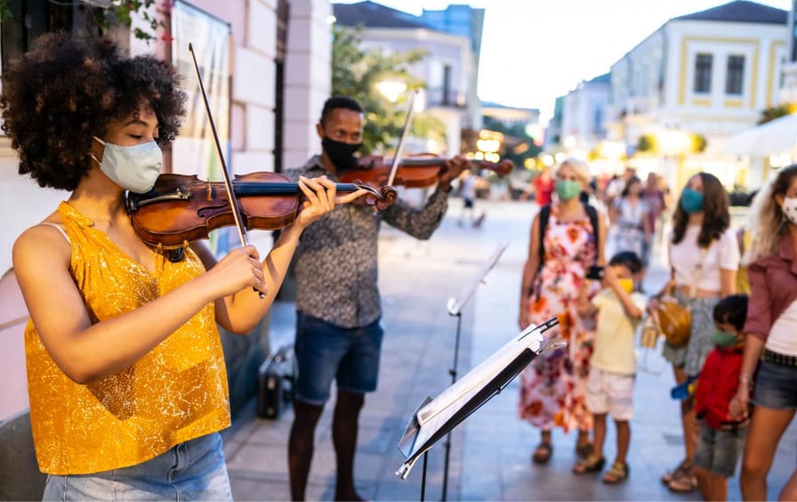 Two violinists play music in the street as young families listen