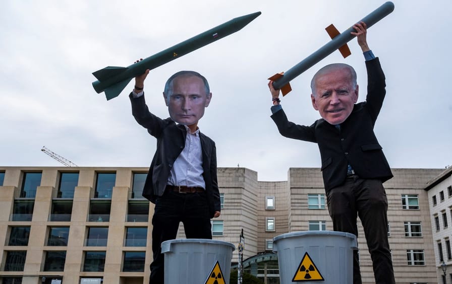 Protesters dressed with cutout faces of Biden and Putin prepare to throw nuclear weapons in the garbage