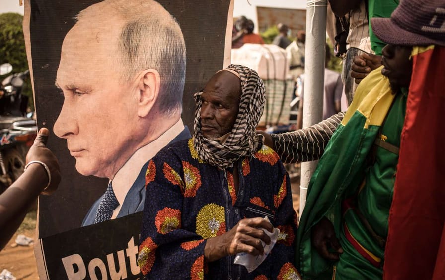 A man sits in front of an image of Vladimir Putin