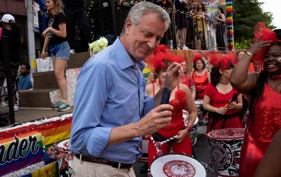 Bill De Blasio grooves in front of drummers dressed in red.