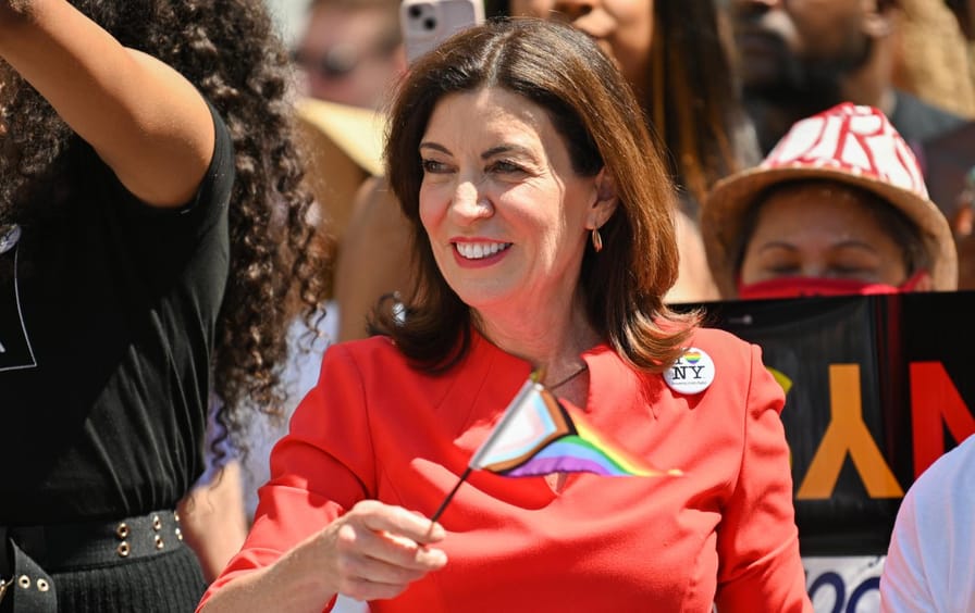 Kathy Hochul, in red, waves a Pride flag.
