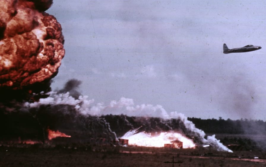 A jet flies with a napalm explosion behind it.
