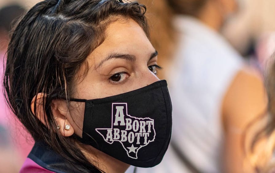 A woman wears a mask in reference to Texas Governor that says 