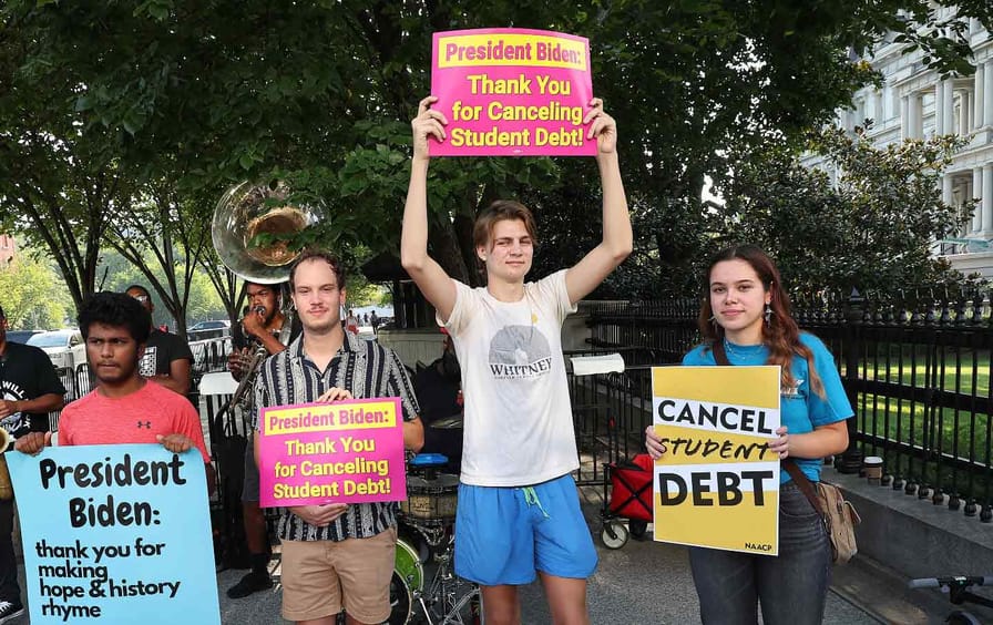 Four student loan borrowers stage a rally holding signs in front of The White House to celebrate President Biden’s canceling student debt