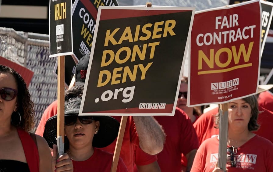 Kaiser Permanente mental health workers and supporters march outside a Kaiser facility in Sacramento, Calif. holding picket signs and wearing union shirts.
