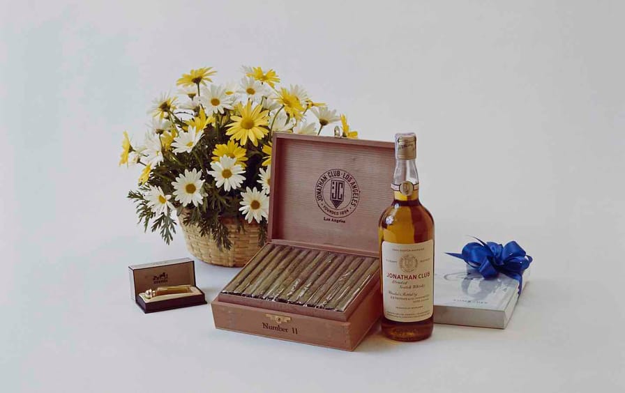 Whisky bottle with cigar and flower on white background