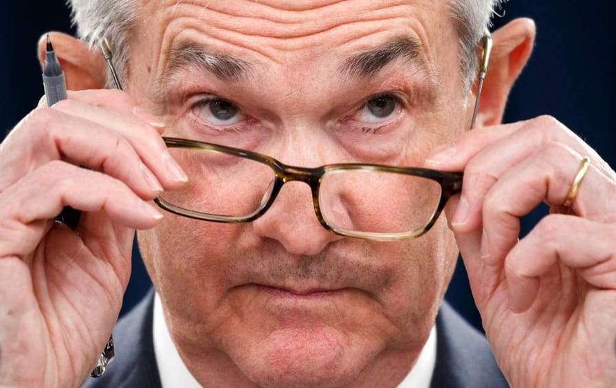 A closeup of Federal Reserve Chair Jerome Powell removing his glasses during a news conference.