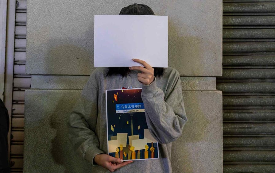 A protester in Hong Kong holds up a sign and a blank piece of paper in solidarity with people protesting zero-Covid policies in mainland China