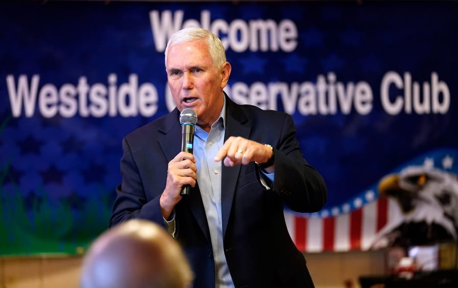 Mike Pence speaking into a microphone in front of a sign reading 