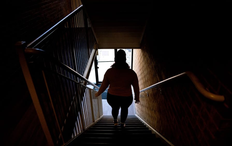 A woman, seen in silhouette, works down a staircase in a home.