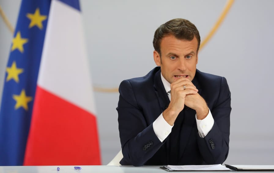 Emmanuel Macron sits at a table during a live address