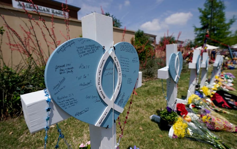 Crosses with hearts on them and names and messages written on them in a row, memorializing the victims of the mass shooting in Allen, Texas.