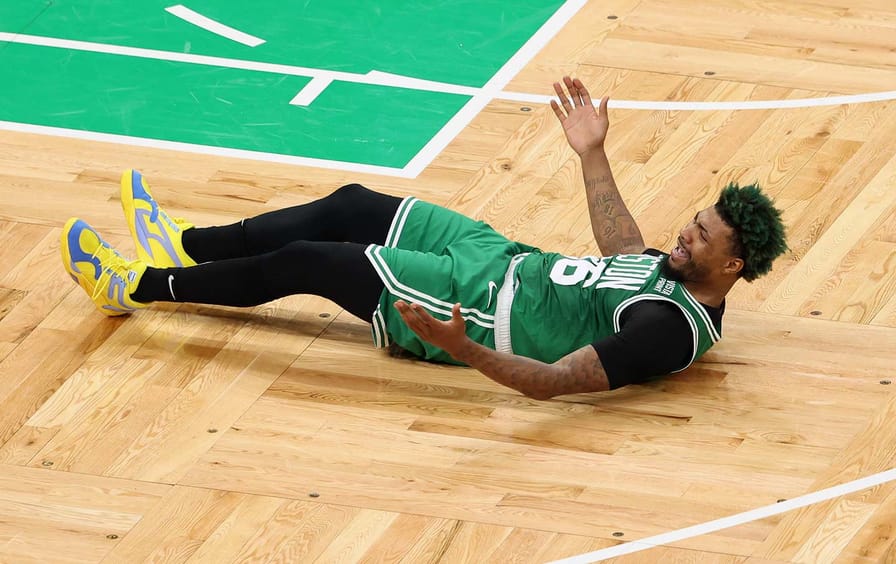 Marcus Smart, a Celtics player, lies on the hardwood, frustrated—hands up.
